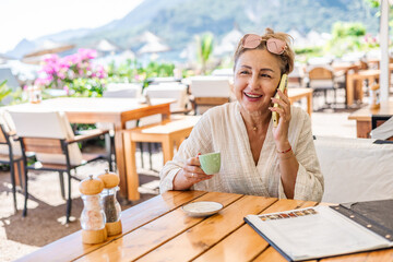 Middle-aged woman with phone sitting at table in beach restaurant