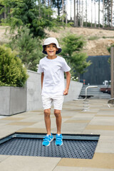 boy jumps on trampoline, wearing white t-shirt, shorts, bucket hat