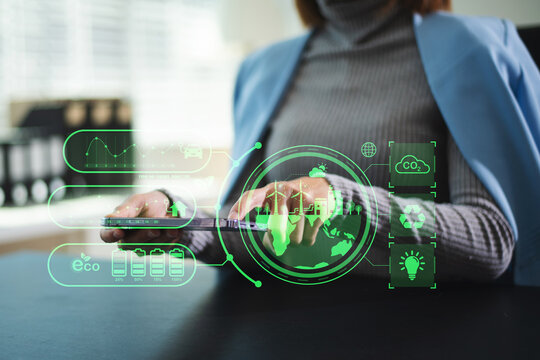 Woman using futuristic interface with smart tech and mobile to manage ESG, clean energy, and sustainability data. in office - Powered by Adobe