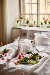 Reading in a bed surrounded by flowers in a cozy room
