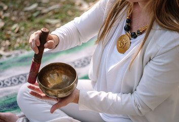 Woman meditating with singing bowl for sound healing outdoors