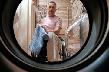 A man in a wheelchair placed washed towels from the washing machine on his lap.