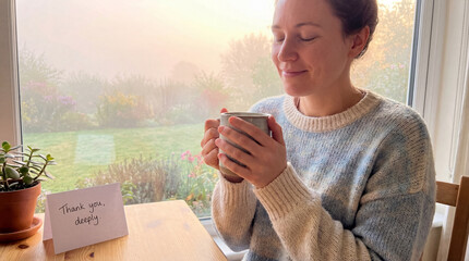 A radiant woman pauses in the morning light, drinking tea. A card reading Thank you, deeply. sits on the table, conveying appreciation and sparking a feeling of profound gratitude.