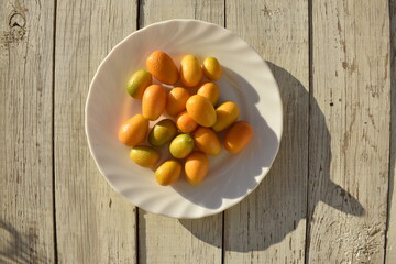 White plate with fresh kumquat harvest on white wooden background, top view