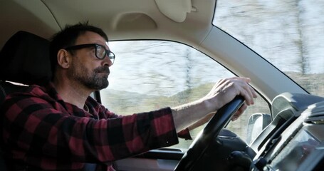 Side view of driver looking out: A man in a plaid shirt checks his surroundings on a rural mountain road.