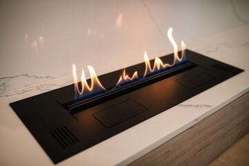 Obraz premium Burning eco bio ethanol fireplace built into white marble. Automatic tabletop biofireplace. Beautiful marble fireplace. Minimalist interior, alternative bio fireplot fireplace on ethanol gas.