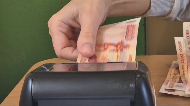 Money verification rubles, cashier using currency detector machine to check authenticity of Russian 5000 Ruble banknotes, transaction concept.