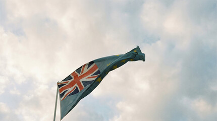 A flag featuring the Union Jack and European stars waves against a backdrop of soft, cloudy skies.