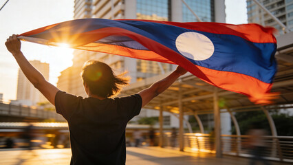 Silhouette of a person proudly holding the Laotian flag against a colorful sunset, ideal for celebrating national pride in media or social posts.
