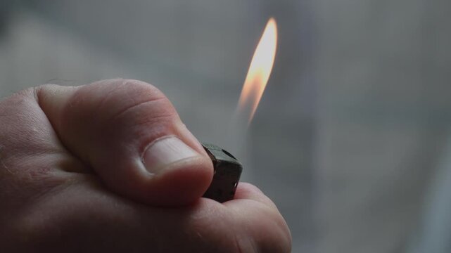 Close up of a hand holding a lighter and the moment it ignites indoors