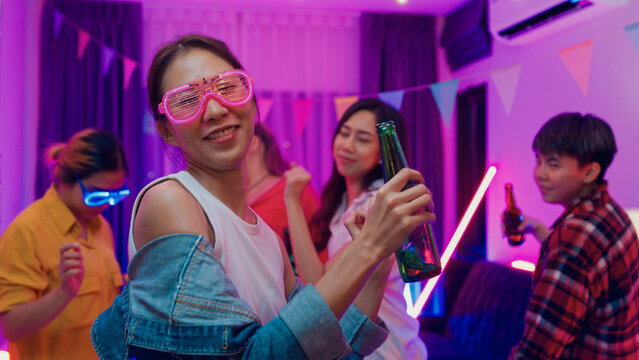 Diverse group multiethnic young adult Asia friend wear futuristic neon glowing glasses dance and drink alcohol beer fun hangout party in living room night indoor home. Disco lights illuminating house. - Powered by Adobe