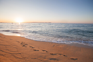 Golden sand with footprints, gentle waves at sunset on tranquil coastal shoreline