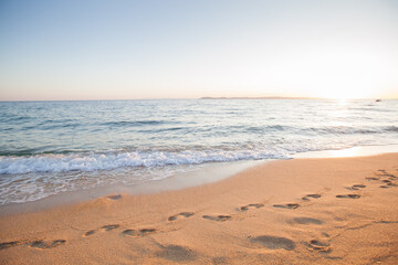 Golden sand with footprints, gentle waves at sunset on tranquil coastal shoreline