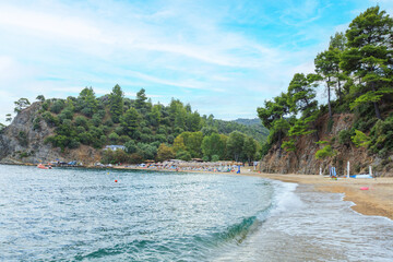 Scenic beach with clear water, lush hills, and relaxing visitors under a bright sky