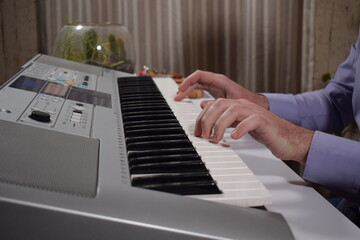 A young white man plays an electronic synthesizer indoors, immersed in his creative hobby. Focused on shaping tones and melodies, he explores musical expression and artistry in a calm home setting.
