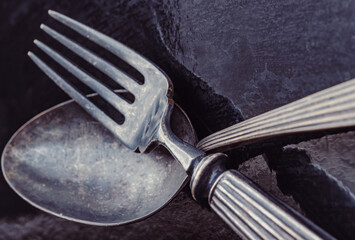 Close-up of Ancient worn vintage cutlery on the dark background. Crossed black metal spoon and fork in dark tone, Highlighting its texture and design, use it as your Wallpaper, Poster and Copy space S