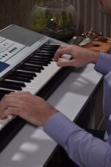 A young white man plays an electronic synthesizer indoors, immersed in his creative hobby. Focused on shaping tones and melodies, he explores musical expression and artistry in a calm home setting.
