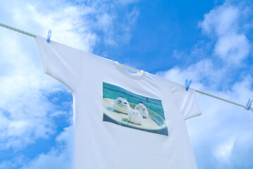 A clean white T-shirt with a cute rice ball illustration hangs on a clothesline against a bright blue sky, creating a fresh and cheerful lifestyle scene perfect for design and copy space
