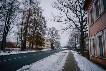 Rujiena, Latvia - November 27, 2025: Winter street scene with snow-covered sidewalk and trees lining the road in a quiet residential area
