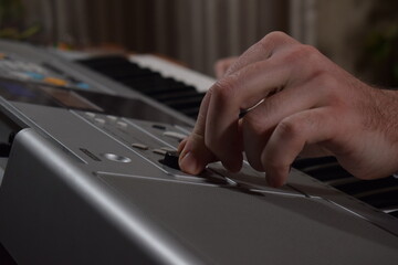 A young white man plays an electronic synthesizer indoors, immersed in his creative hobby. Focused on shaping tones and melodies, he explores musical expression and artistry in a calm home setting.
