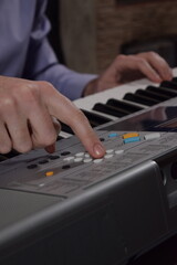 A young white man plays an electronic synthesizer indoors, immersed in his creative hobby. Focused on shaping tones and melodies, he explores musical expression and artistry in a calm home setting.
