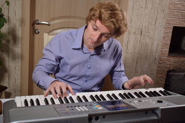 A young white man plays an electronic synthesizer indoors, immersed in his creative hobby. Focused on shaping tones and melodies, he explores musical expression and artistry in a calm home setting.
