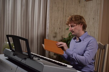 A young white man plays an electronic synthesizer indoors, immersed in his creative hobby. Focused on shaping tones and melodies, he explores musical expression and artistry in a calm home setting.
