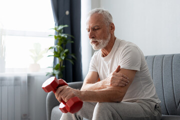 Senior man experiencing arm pain while exercising with a dumbbell at home