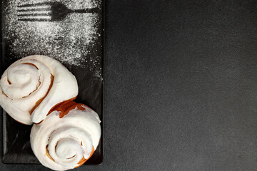 Fragrant cinnabons with cream on a black rectangular plate on a gray background