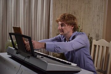 A young white man plays an electronic synthesizer indoors, immersed in his creative hobby. Focused on shaping tones and melodies, he explores musical expression and artistry in a calm home setting.
