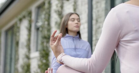 Woman instructor lifting smartwatch hand, guiding woman student breathing deeply on patio for calm
