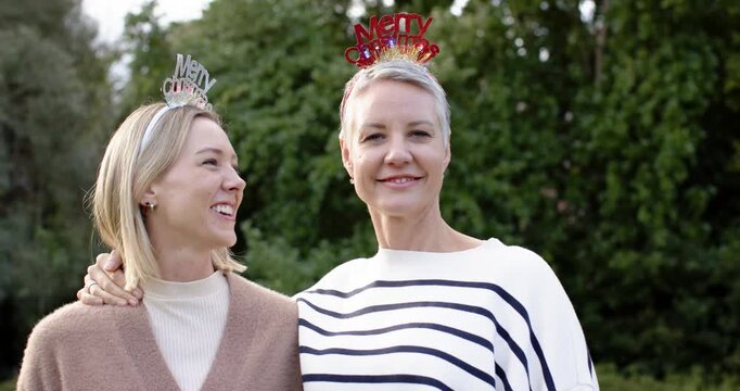 Entering garden mother and daughter wearing Xmas headbands embracing and giggling in festive joy