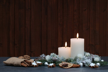 Christmas background: White candles with Christmas decorations and fir branches in front of a wooden background with space for text.