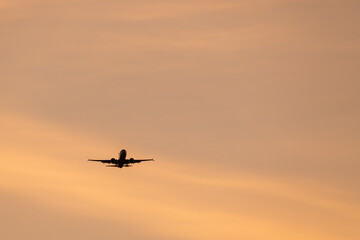 Silhouette of commercial passenger airplane landing with gear down against beautiful golden orange sunset sky background with copy space.