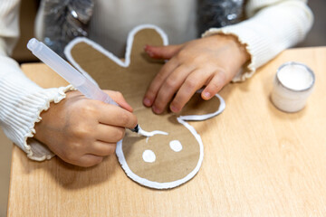 Little girl's hands, child decorating, painting gingerbread man made from cardboard. Christmas preparation. Concept of eco holiday, New year eve, family, motherhood and childhood