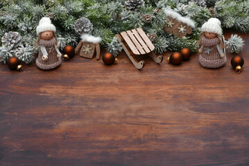 Obraz premium Christmas background: Christmas scene with small dolls, sleds, fir branches and Christmas decorations on a wooden background with space for text.