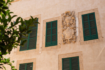 Ornate Stone Plasterwork Featuring a Coat of Arms on a Pale Facade with Green Shutters, Palma