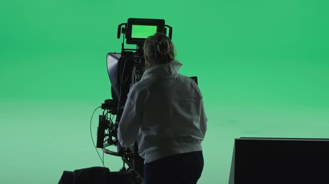 Woman camera operator preparing for shooting in a green screen studio