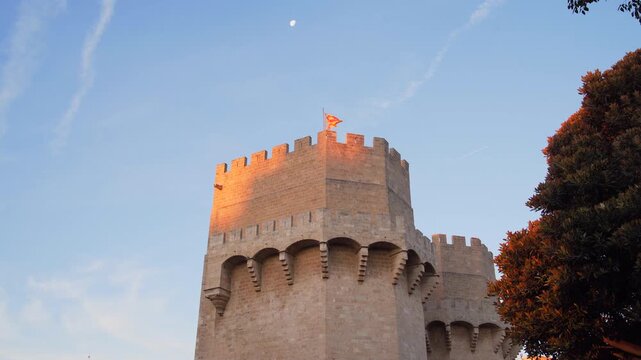 Torres de serranos, part of valencia's ancient city walls, showcasing a historic landmark in golden morning light with the moon.