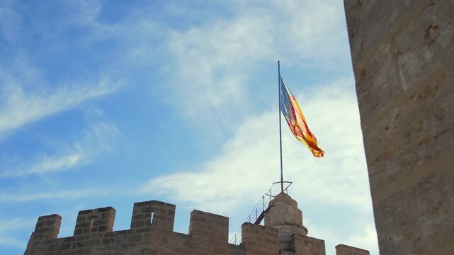 Valencian community flag waving on the serranos towers, a historic gateway and landmark in valencia, spain, under a blue sky.