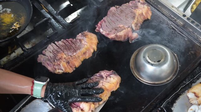 Chef cooking sliced tagliata steak on a hot griddle