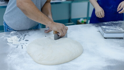 Unknown hand people knead fresh dough on floured stainless steel table in clean food preparation area, Factory production line baking preparation professional kitchen workflow industrial technology.