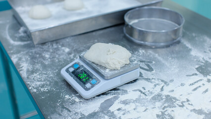 Fresh dough weigh flour on digital scale rests on stainless steel table in clean food preparation area, Factory production line baking preparation professional kitchen workflow industrial technology.