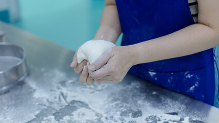 Unknown hand people knead fresh dough on floured stainless steel table in clean food preparation area, Factory production line baking preparation professional kitchen workflow industrial technology.