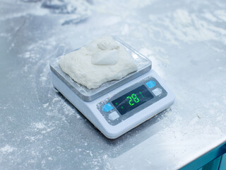 Fresh dough weigh flour on digital scale rests on stainless steel table in clean food preparation area, Factory production line baking preparation professional kitchen workflow industrial technology.