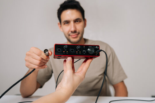 Portrait of young sound engineer male connecting xlr cable to red usb audio interface, recording music with sound card equipment and headphones for professional studio work and podcasting.