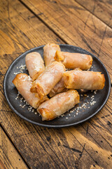 Fried spring rolls snack food on black plate with sesame topping overhead wooden background