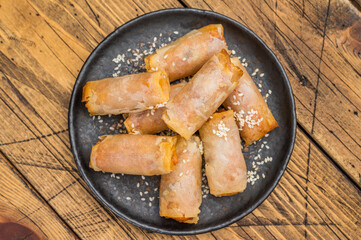 Crispy fried Egg rolls with sesame seeds on dark ceramic plate rustic wooden background top view