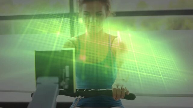 Woman on rower driving legs pulling handle and checking console, green overlay tracking fitness