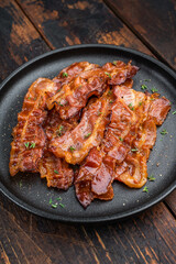 Crispy sizzling bacon with glossy caramel surface served on a dark plate over rustic wood creating rich appetizing food style.